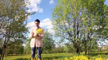 Kız bir buket çiçek açan kolza tohumu topluyor. Bahar çiçekli çayırların arasında. Güneşli serin hava..