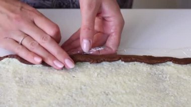 Bir kadın hindistancevizi karışımı katılmış kahverengi bir hamur topağını yuvarlıyor. Tatlı yapmak için gerekli malzemeler.