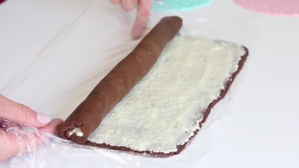 Une femme roule un morceau de pâte brun déployé avec un mélange de noix de coco. Ingrédients pour la fabrication du dessert — Video