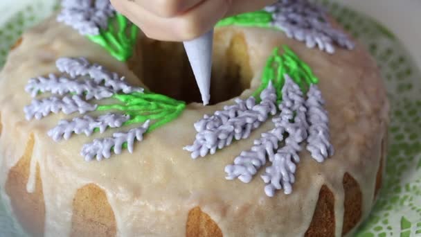 La donna dipinge fiori di lavanda con smalto. Su un cupcake con glassa di zucchero. Primo piano. — Video Stock