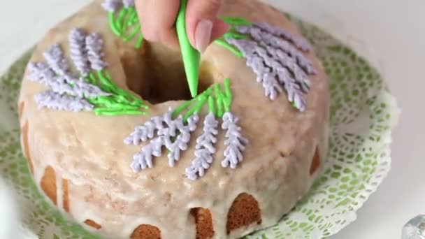 Zuckerkuchen. Frau zeichnet Lavendelblüten auf einen Cupcake. Mit Zuckerguss, mit einer Teigtasche. Nahaufnahme. — Stockvideo