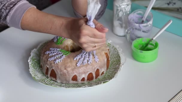 Suikerkoekje. Vrouw tekent lavendelbloemen op een cupcake. met glazuur, met behulp van een banketzak. — Stockvideo