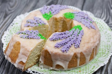 Lavantalı kek. Şeker kaplı. Lavanta rengi çiçeklerle süslenmiş. Küçük bir parça kesilmiş..
