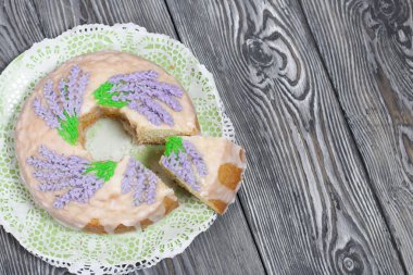 Lavantalı kek. Şeker kaplı. Lavanta rengi çiçeklerle süslenmiş. Küçük bir parça kesilmiş..