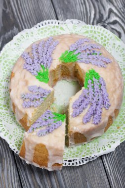 Lavantalı kek. Şeker kaplı. Lavanta rengi çiçeklerle süslenmiş. Küçük bir parça kesilmiş..