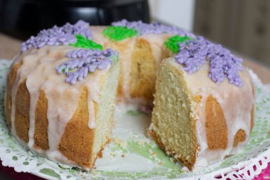 Lavantalı kek. Şeker kaplı. Lavanta rengi çiçeklerle süslenmiş. Küçük bir parça kesilmiş..