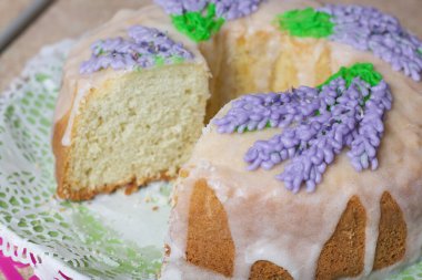Lavantalı kek. Şeker kaplı. Lavanta rengi çiçeklerle süslenmiş. Küçük bir parça kesilmiş..