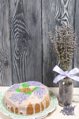 Lavantalı kek. Şeker kaplı. Lavanta rengi çiçeklerle süslenmiş. Lavanta kabartması ve buketle bankanın yanında..