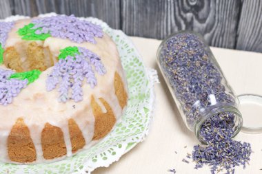 Lavantalı kek. Şeker kaplı. Lavanta rengi çiçeklerle süslenmiş. Lavanta kabartılarıyla bankanın yanında..