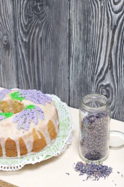 Lavantalı kek. Şeker kaplı. Lavanta rengi çiçeklerle süslenmiş. Lavanta kabartılarıyla bankanın yanında..