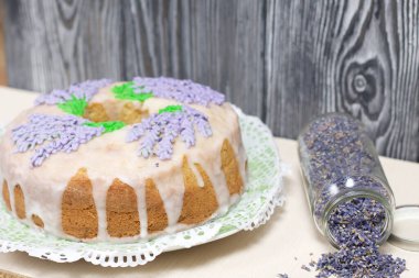 Lavantalı kek. Şeker kaplı. Lavanta rengi çiçeklerle süslenmiş. Lavanta kabartılarıyla bankanın yanında..