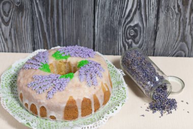 Lavantalı kek. Şeker kaplı. Lavanta rengi çiçeklerle süslenmiş. Lavanta kabartılarıyla bankanın yanında..