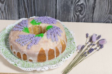 Lavantalı kek. Şeker kaplı. Lavanta rengi çiçeklerle süslenmiş. Bir demet lavantanın yanında..
