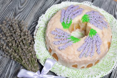 Lavantalı kek. Şeker kaplı. Lavanta rengi çiçeklerle süslenmiş. Bir demet lavantanın yanında..