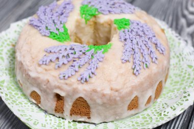 Lavantalı kek. Şeker kaplı. Lavanta rengi çiçeklerle süslenmiş. Küçük bir parça kesilmiş..