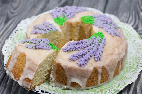 Lavantalı kek. Şeker kaplı. Lavanta rengi çiçeklerle süslenmiş. Küçük bir parça kesilmiş..