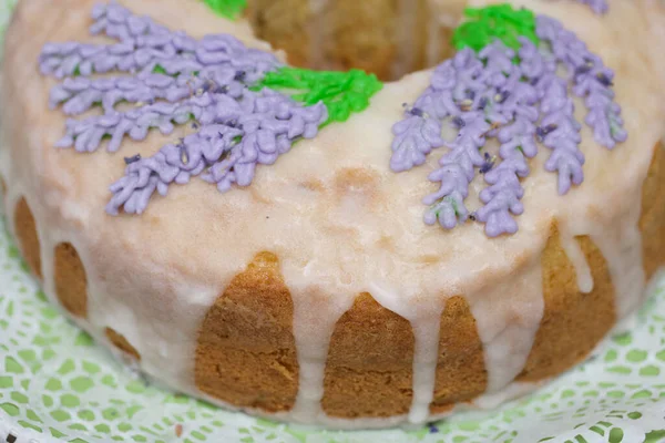 Lavantalı kek. Şeker kaplı. Lavanta rengi çiçeklerle süslenmiş. Küçük bir parça kesilmiş..