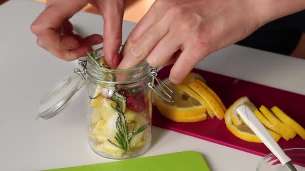Η γυναίκα βάζει δεντρολίβανο, φέτες λεμονιού, πιπέρι και αλάτι σε ένα γυάλινο βάζο. Αναμιγνύει συστατικά αλάτισης λεμόνι — Αρχείο Βίντεο