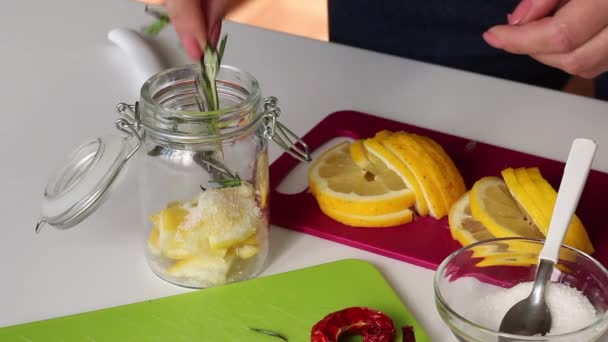 女人把迷迭香,柠檬片和盐放在玻璃瓶里.靠近迷迭香，盐和辣椒。腌制柠檬的配料. — 图库视频影像