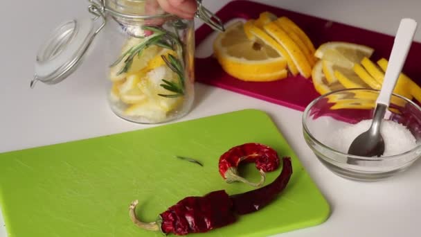 Vrouw doet rozemarijn, citroenschijfjes en zout in een glazen pot. Vlakbij rozemarijn, zout en hete peper. Ingrediënten voor zalmcitroen — Stockvideo