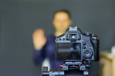 Bir blogcu kendini kameraya alır. Kamerasına bir tripoda odaklan. Selamlaşmanın işareti. Diğer her şey bulanık..