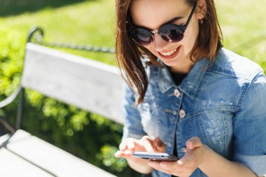 Güzel neşeli kız parkta oturan bir akıllı telefon ile bir