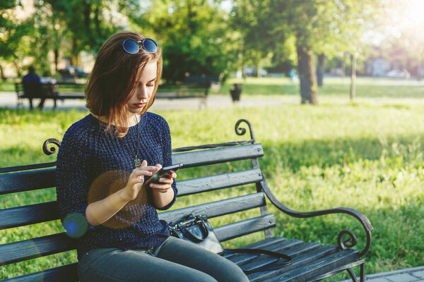 Красивая счастливая девушка переписывается в социальных сетях в парке на
 