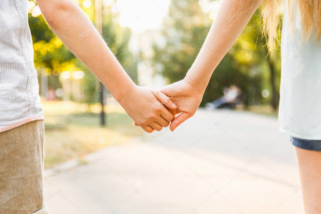 young boy and girl hold hands and stroll in the park in sunny we