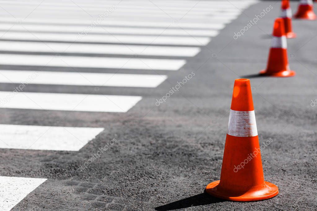 orange traffic cones standing in a row near the pedestrian cross