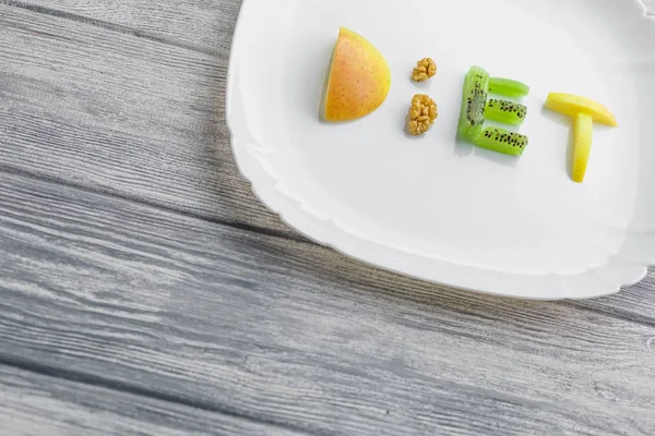 Fruits sur une assiette d'un mot régime alimentaire de pomme, kiwi, carottes, noix et — Photo