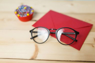 Masada gözlük ve kek olan kırmızı zarf.