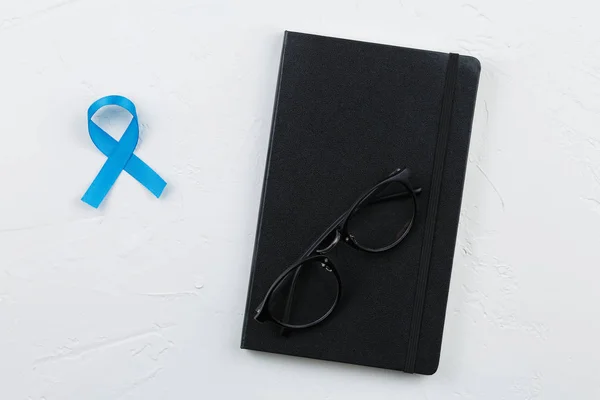 Notebook with blue prostate cancer ribbon on white textured table