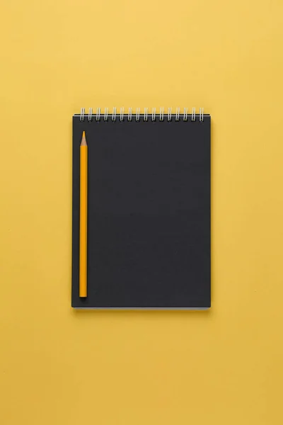 Notebook met zwart papier en potlood op een gele achtergrond bovenaanzicht — Stockfoto