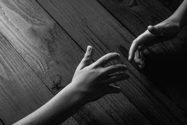 Руки розтягуються і тримаються один з одним на чорному дерев'яному фоні. чорно-білий . — стокове фото