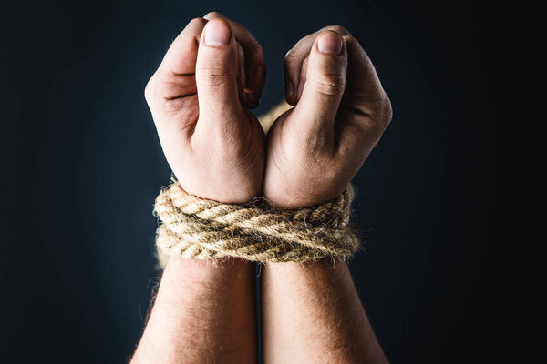 hands tied with rope on black background