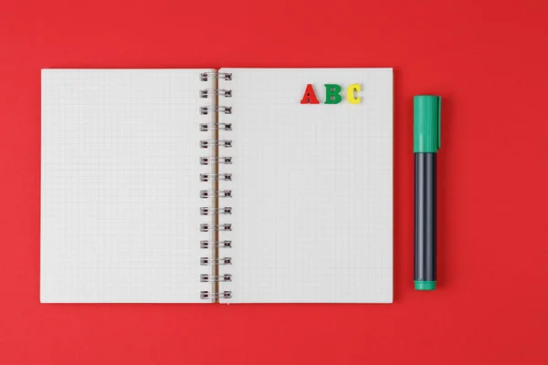 Notebook with ABC letters and colored markers on a red background