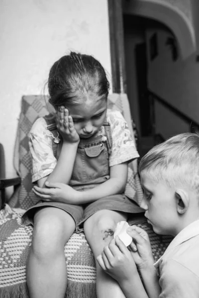 little girl hurt her knee, a boy heals her wound.black and white.