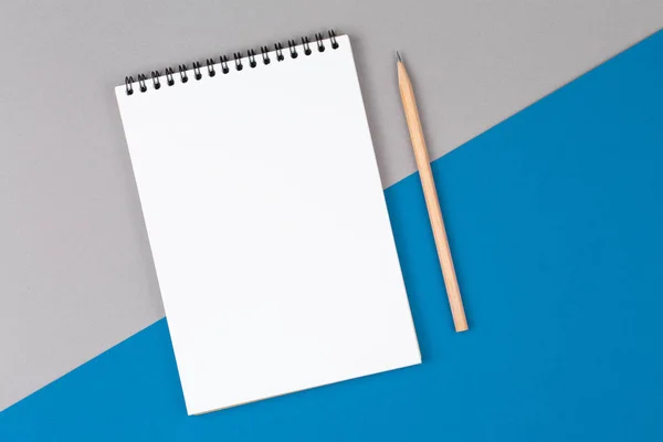 Cuaderno con lápiz sobre tabla azul y gris vista superior, con página en blanco —  Fotos de Stock