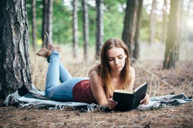 Kadın ağacın altında doğada okuyor.