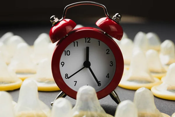 Despertador vermelho com preservativos no fundo preto — Fotografia de Stock