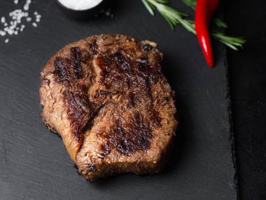 Siyah tabakta kızarmış biftek ve masada baharatlar.