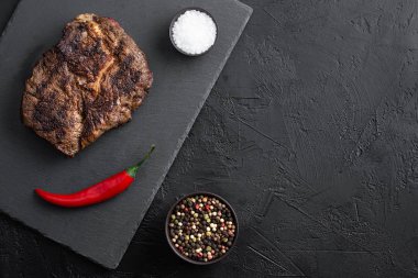 Siyah tabakta kızarmış biftek ve masada baharatlar.