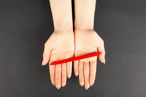 Penna rossa in mano su sfondo nero, vista dall'alto . — Foto Stock