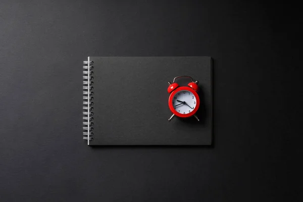 Caderno aberto com despertador vermelho no preto — Fotografia de Stock