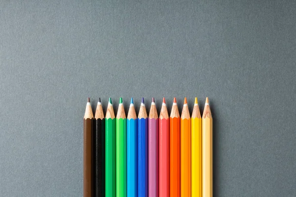 Colored pencils in row on gray background top view — Stock Photo, Image