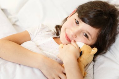 Tatlı kız beyaz yatakta yumuşak oyuncaklarla yatıyor.