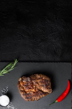Tabakta kızarmış biftek ve siyah masada baharatlar.