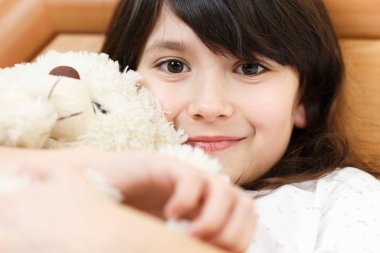 Tatlı kız beyaz yatakta yumuşak oyuncaklarla yatıyor.