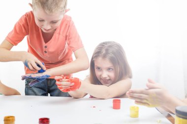 Çocuklar ellerini masaya koyup resim yaparlar.