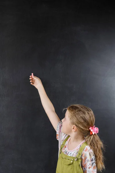 Mała dziewczynka wskazuje na pustą tablicę. — Zdjęcie stockowe